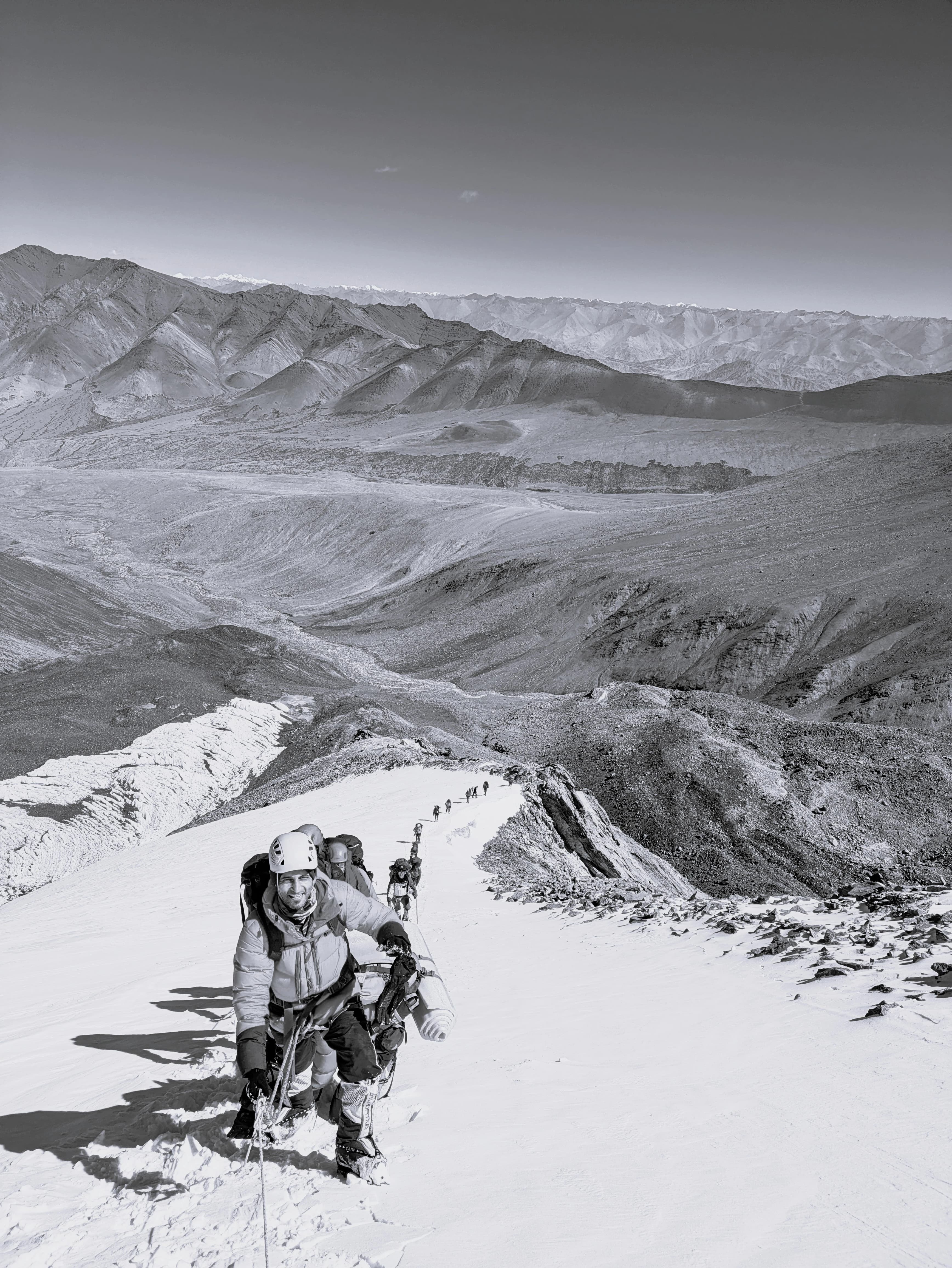 A climber at the head of a roped line, turning back toward the camera on a snow ridge